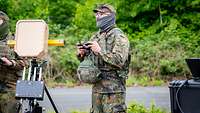 Ein Soldat mit Fernsteuerung in der Hand blickt in den Himmel zur von ihm gesteuerten Drohne.