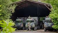 Drei große Militär-LKW rangieren in den Flugzeughangar hinein.
