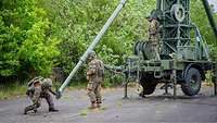 Eine Gruppe von Soldaten baut die Stützen der hohen TETRAPOL-Antenne auf.