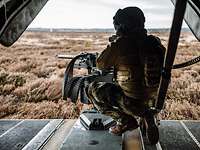 Ein Soldat beobachtet von der Heckklappe eines Helikopters schussbereit das Gelände vor ihm