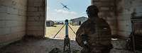 Ein Soldat kniet neben einer Startrampe in einem Gebäude und draussen fliegt eine Drohne.