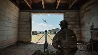Ein Soldat kniet neben einer Startrampe in einem Gebäude und draussen fliegt eine Drohne.