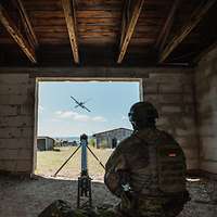 Ein Soldat kniet neben einer Startrampe in einem Gebäude und draussen fliegt eine Drohne.