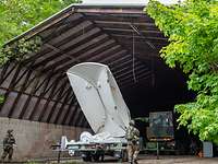 Soldaten bauen in einem Hangar eine große weiße Satellitenschüssel auf.