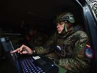 Ein Soldat sitzt vor einem Laptop und berührt mit seinem Finger den Bildschirm.