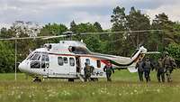 Soldaten und Zivilisten laufen über eine Wiese zu einem Hubschrauber.