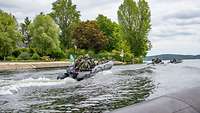 Mehrere Schlauchboote voll besetzt in schneller Fahrt auf einem Fluss.