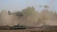 Über einem Kampfpanzer schweben Hubschrauber.