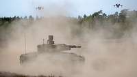 Ein Schützenpanzer Puma fährt durch sandiges Gelände, über dem Drohnen schweben.