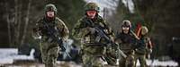 Bewaffnete Soldaten laufen im verschneiten Gelände.