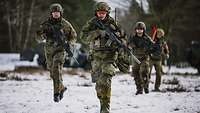Bewaffnete Soldaten laufen im verschneiten Gelände.