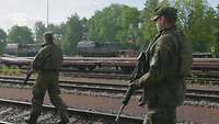 Zwei bewaffnete Soldaten gehen Gleisen entlang auf einem Bahngelände.