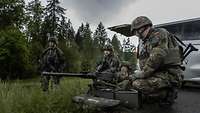 Soldaten knien auf einer Wiese an einer Straße um ein Schweres Maschinengewehr am Auto.