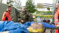 2 zivilie Rettungskräfte halten eine Puppe auf einer Trage, ein Soldat erklärt etwas
