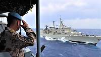 Ein Soldat macht einen militärischen Gruß zu einem griechischen Kriegsschiff