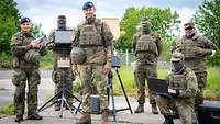 Eine Soldatin hält eine Drohne in den Händen, zwischen weiteren Personen stehen Störsender.
