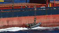 Soldaten steigen von einem Schnellboot über eine Strickleiter auf ein ziviles Frachtschiff über