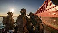 Drei Soldaten auf einem Speedboot, die vor einem großen zivilen Handelsschiff stehen