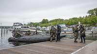 2 Schlauchboote im Wasser. Soldaten und Zivilisten sind auf dem Steg und sitzen in Booten