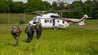 Soldaten und zivile Personen mit Schutzwesten laufen auf einer Wiese auf einen Hubschrauber Cougar zu.