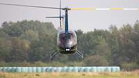 Ein Hubschrauber im Flug dicht über dem Boden. Zwei Personen sitzen im Cockpit.