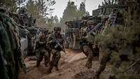 Viele Soldaten mit Gewehren rennen zwischen Schützenpanzern, die auf einem Sandweg stehen.