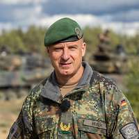 Ein Soldat steht auf einem Feld vor drei Schützenpanzern.
