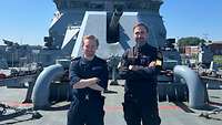 Ein deutscher und ein britischer Soldat stehen nebeneinander an Deck eines Militärschiffes und lächeln.