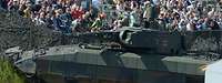 Ein Panzer im Vordergrund und viele Personen im Hintergrund.