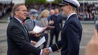 Verteidigungsminister Pistorius gibt einem Soldaten die rechte Hand und hält eine Urkunde in der linken Hand.