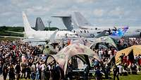 Viele Personen stehen auf einem Ausstellungsgelände. Im Hintergrund sind Flugzeuge zu sehen.