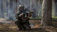 Ein Soldat kniet auf dem brennenden Waldboden mit einer Waffe im Anschlag.