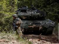Ein Soldat läuft an einem sandigen Waldweg suchend vor einem Panzer.