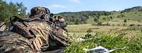 Ein Soldat liegt mit einem Maschinengewehr im Anschlag auf einer Wiese.