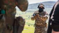 Ein vermummter Soldat steht im Gelände und erklärt etwas.