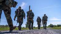Mehrere Soldaten gehen mit ihrer Ausrüstung einen Weg entlang.