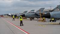Kampfflugzeuge Tornado stehen aufgereiht am Hamburg Airport. Menschen in Warnwesten arbeiten an ihnen.