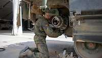 Ein Soldat kniet unter dem Heck eines Panzers und montiert an dessen Kettenantrieb