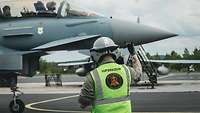 Supervisor in Warnweste dirigiert Eurofighter-Besatzung auf dem Vorfeld