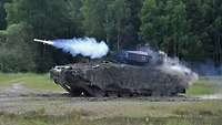 Ein Panzer verschießt einen Lenkflugkörper im Gelände.