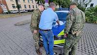 Zwei Soldaten und ein Zivilist blicken auf eine Karte, die auf der Motorhaube eines Polizeiautos liegt.