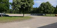 Ein großer betonierter Parkplatz mit viel Wiese und Bäumen drum herum.