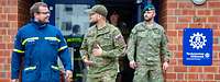 Zwei Soldaten und ein Mensch in Uniform des Technischen Hilfswerks vor einem Gebäude im Gespräch.