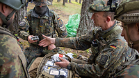 Vier Soldaten in Uniform hocken um einen Rucksack herum, einer von Ihnen zeigt und erklärt etwas.