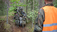 Soldaten verschiedener Nationen in Uniform tragen einen verwundeten einen Hügel runter. 