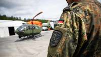 Ein SAR-Hubschrauber davor in Großaufnahme ein Arm eines Soldaten mit Patch.