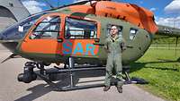 Ein Soldat in Fliegerkombi steht vor einem SAR-Hubschrauber.