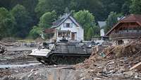 Soldaten fahren auf einem gepanzerten Fahrzeug durch eine vom Hochwasser zerstörte Ortschaft