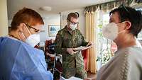 Ein Soldat und zwei Frauen besprechen sich in einem Pflegeheim, im Hintergrund sitzen ältere Menschen