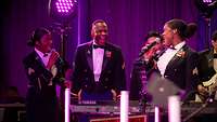 Zwei Frauen und ein Mann in Showuniformen singen gemeinsam.